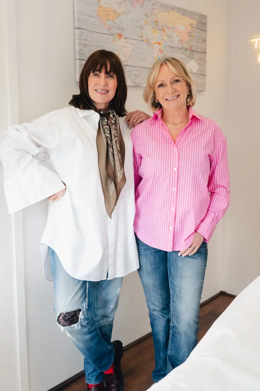 two women standing next to each other in front of a bed