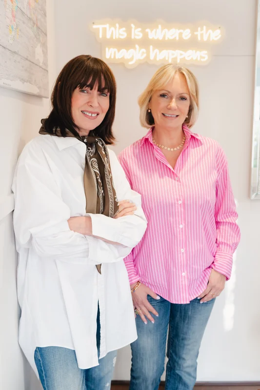 two women standing in front of a sign that says this is where the magic happens