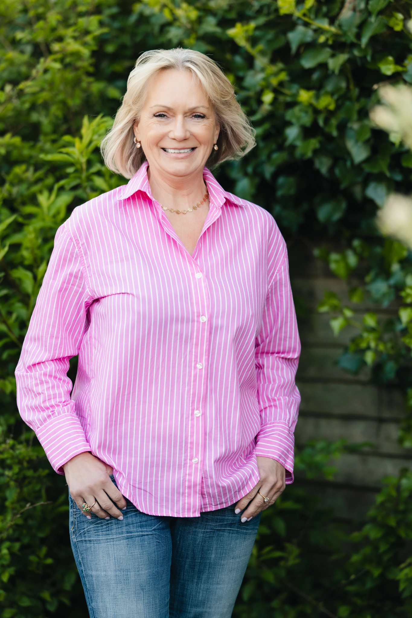 a woman wearing a pink shirt and jeans standing in a garden