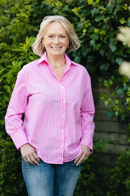 a woman wearing a pink shirt and jeans standing in a garden