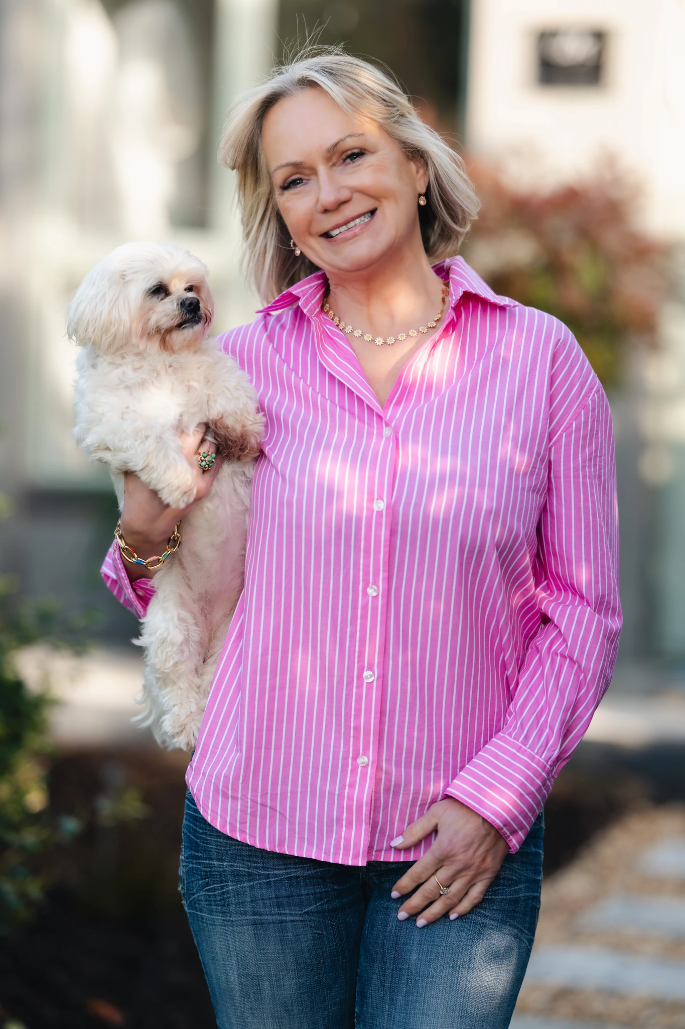 a woman wearing a pink striped shirt and jeans with a dog in the background