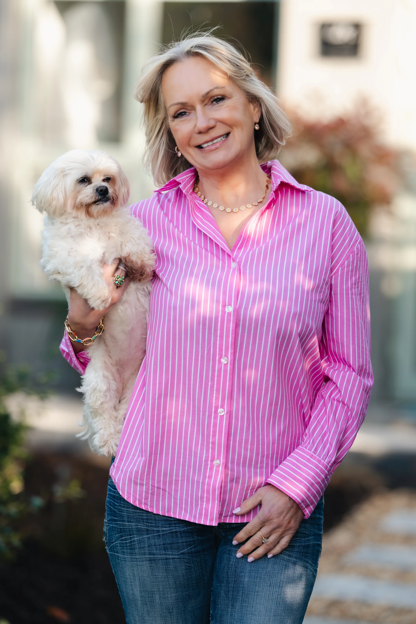 a woman in a pink shirt and jeans holding a small white dog