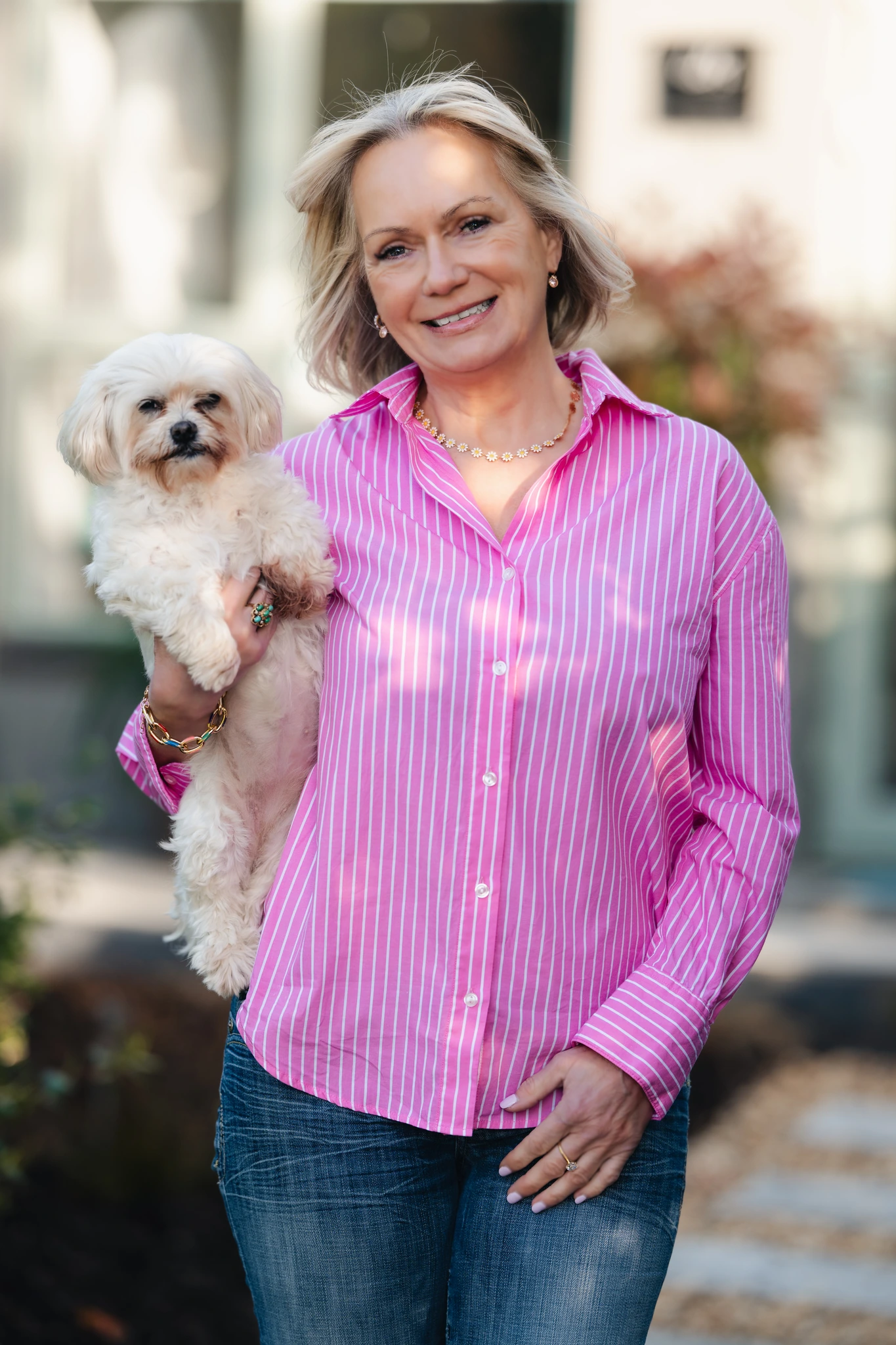 a woman wearing a pink shirt and jeans with a dog in the background