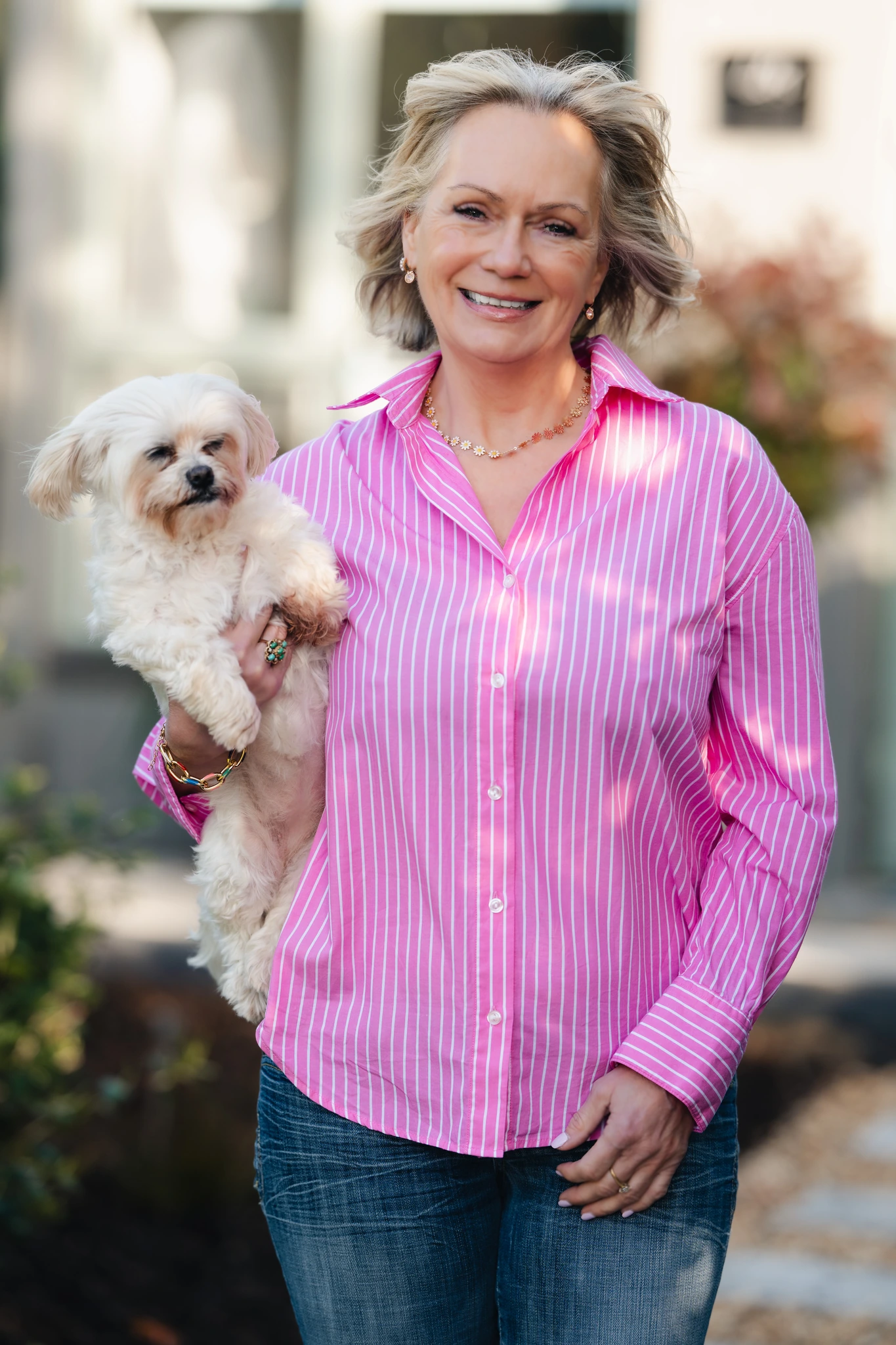 a woman in a pink shirt and jeans holding a small dog in her arms