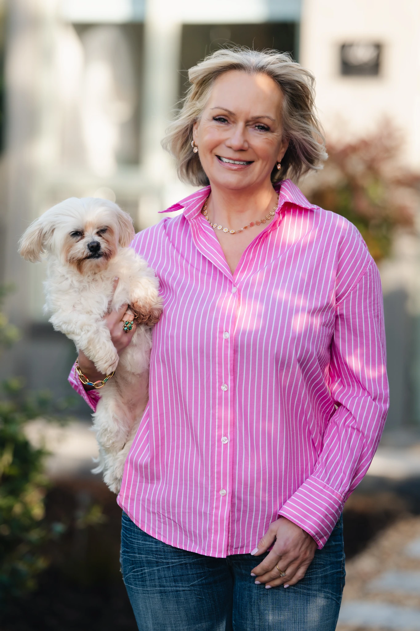a woman in a pink and white shirt holding a small dog in her arms