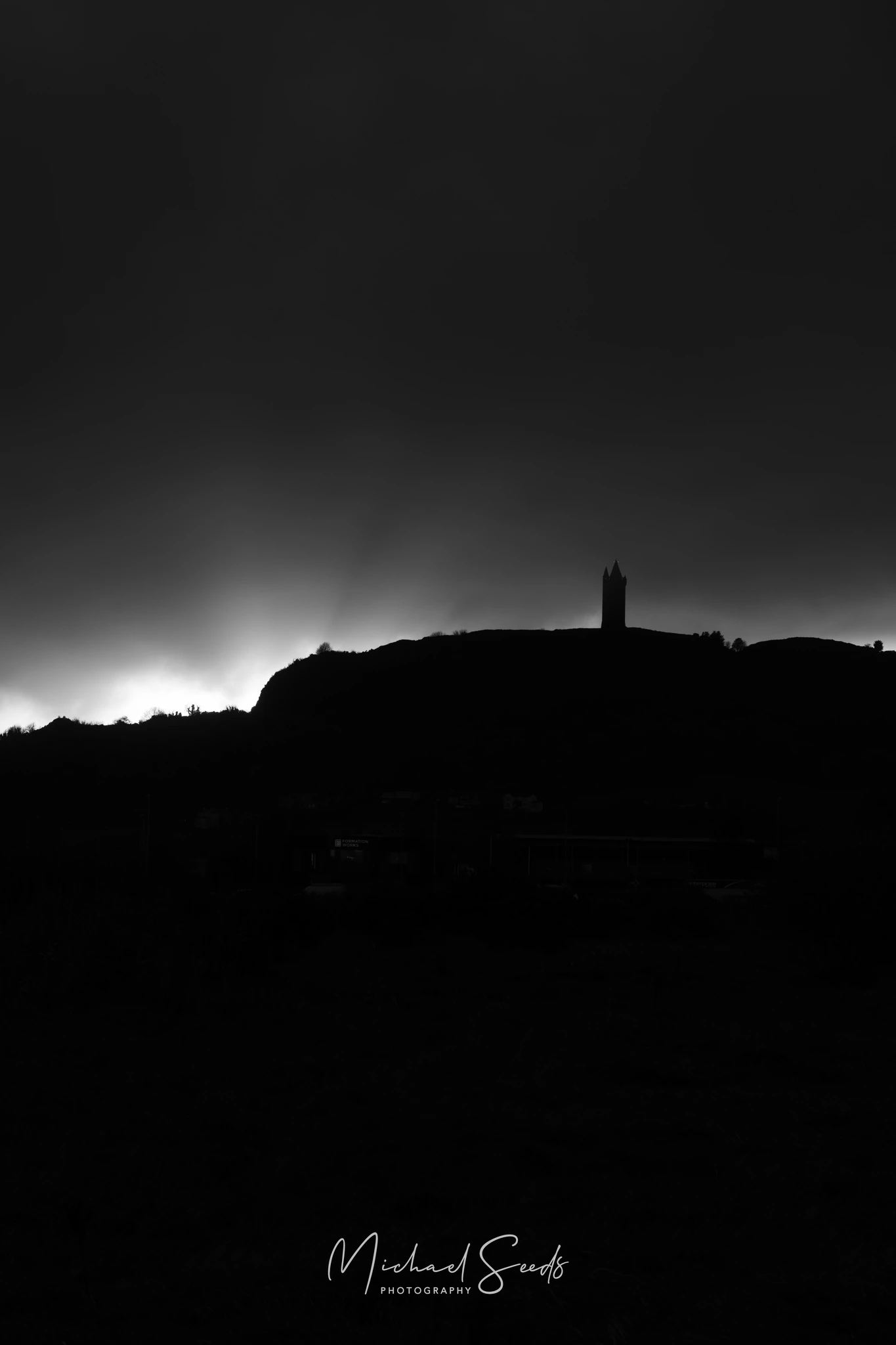 Scrabo Tower stands dark against a fading horizon, a sharp silhouette above the hill. The final light pulls across the landscape before night settles in.