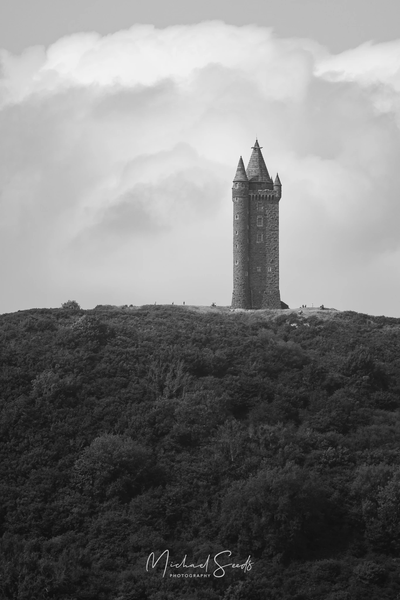 Scrabo Tower rises sharply from the hillside, its scale revealed by the tiny figures walking below. A landmark standing silent over the landscape.