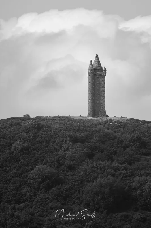 Scrabo Tower rises sharply from the hillside, its scale revealed by the tiny figures walking below. A landmark standing silent over the landscape.