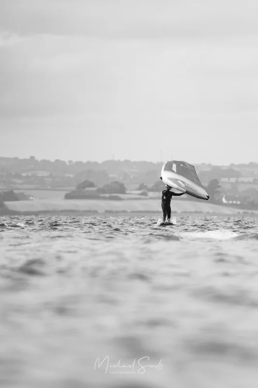 A lone rider glides above the surface, lifted by wind and foil. The blurred water foreground softens the moment into quiet movement.