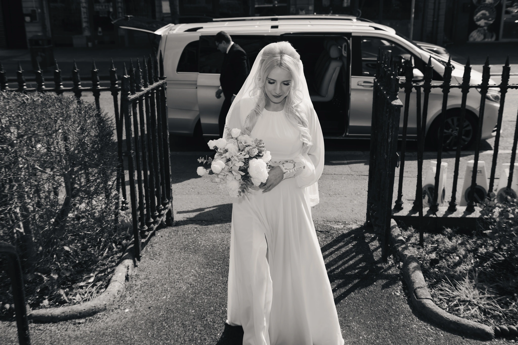 a bride walks down a street with her wedding dress and veil