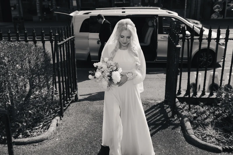 a bride walks down a street with her wedding dress and veil