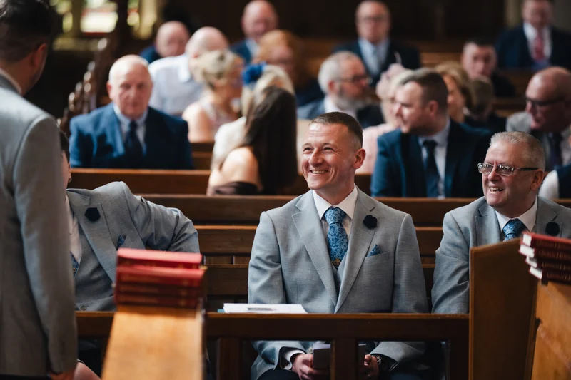 a man in a suit sits on a pew at a wedding ceremony