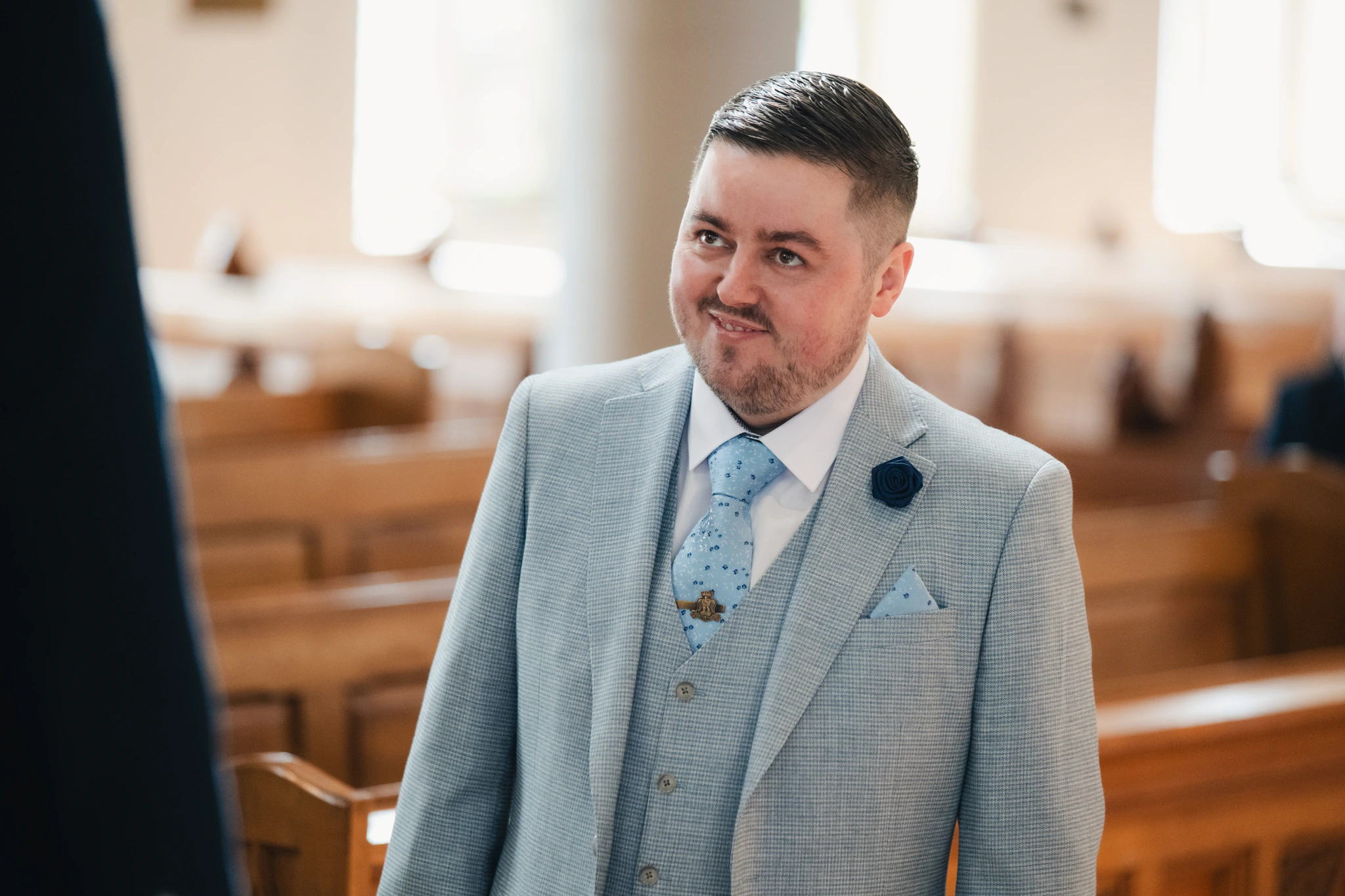 a man dressed in a suit and tie smiles as he walks down the aisle of a church
