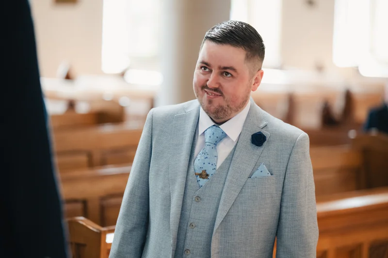 a man dressed in a suit and tie smiles as he walks down the aisle of a church