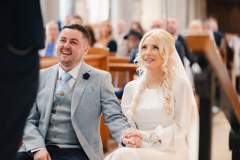 a bride and groom smile as they walk down the aisle of a church