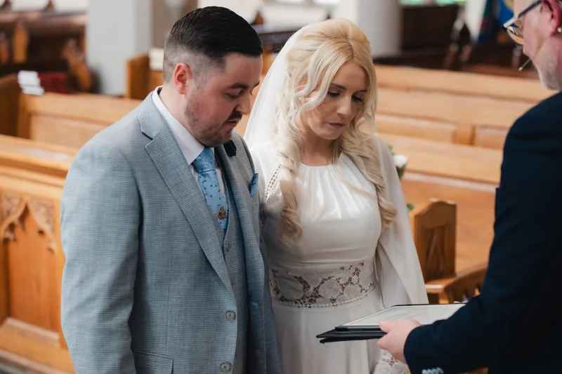 a bride and groom look at their wedding rings as they exchange vows in a church