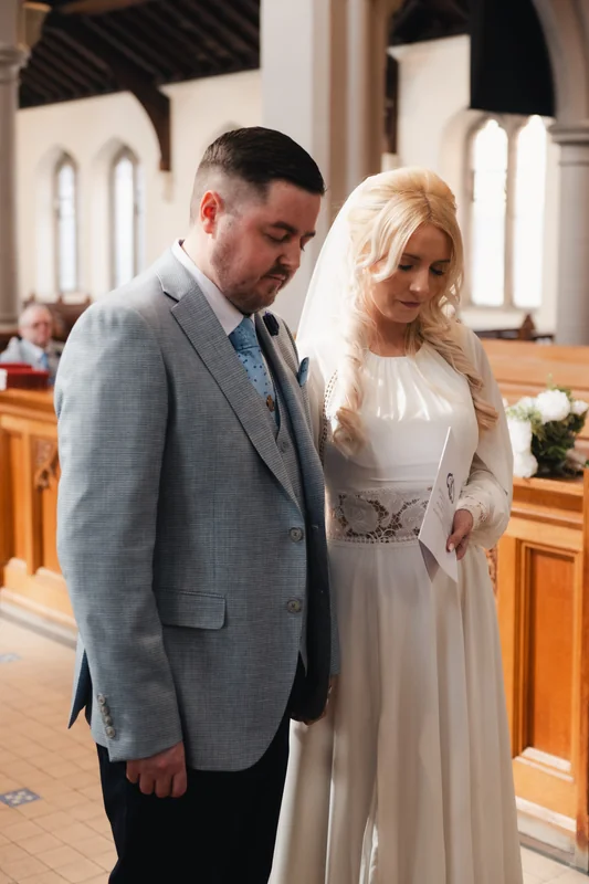 a bride and groom stand in the aisle of a church