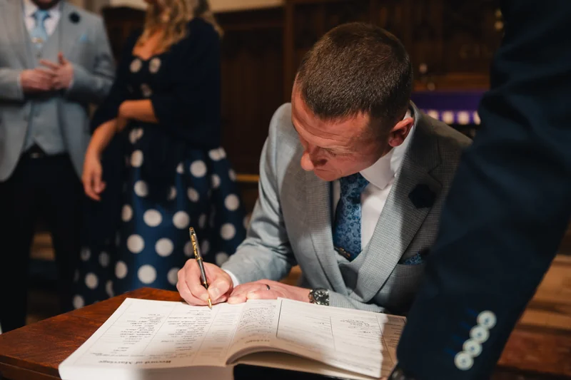 a man signing a wedding book in front of a bride and groom
