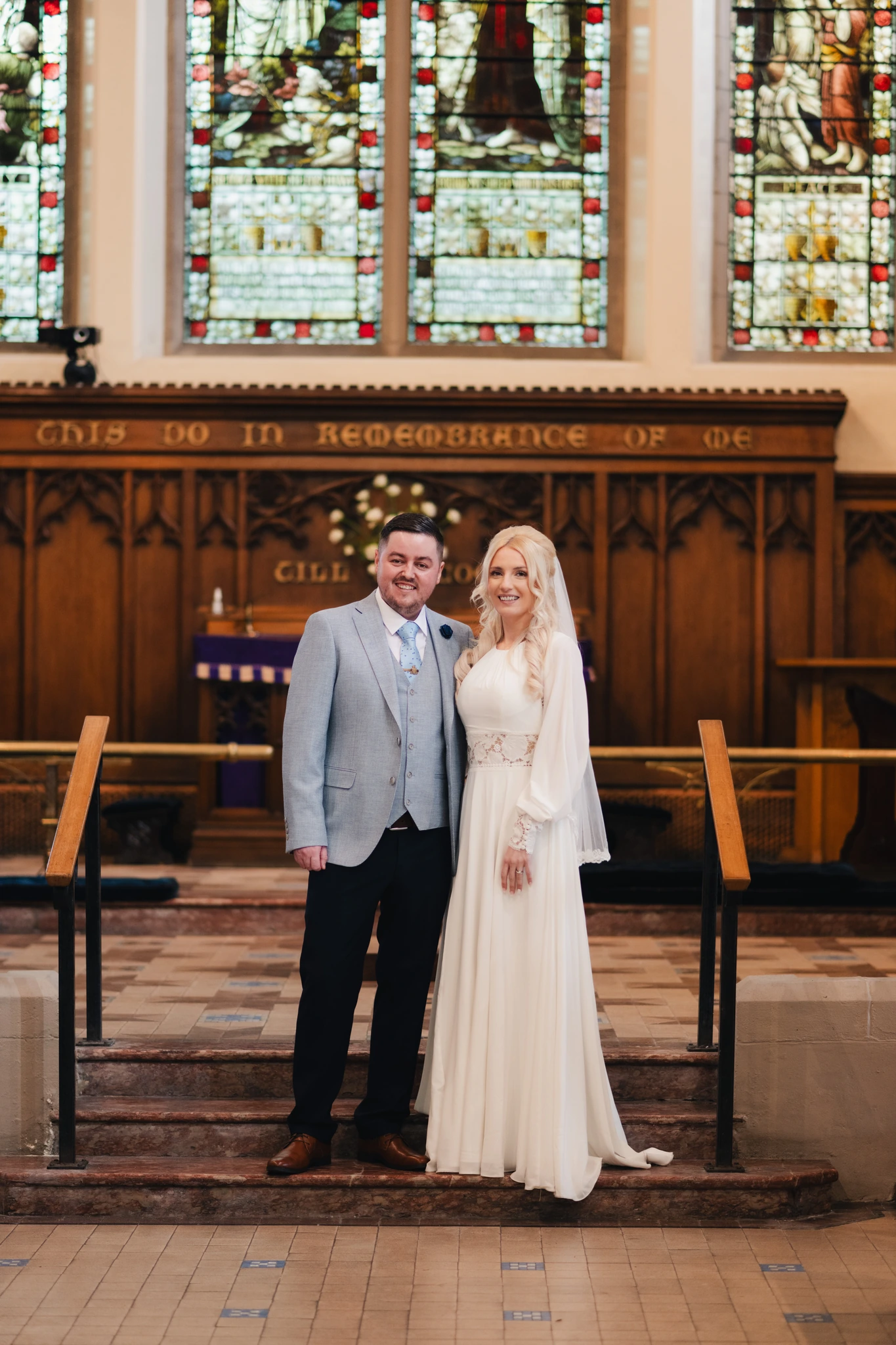 a bride and groom standing in front of a stained glass window