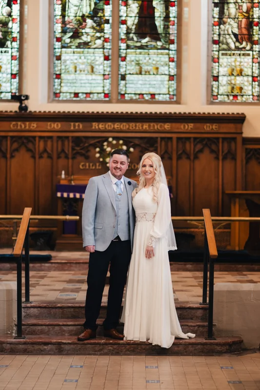 a bride and groom standing in front of a stained glass window
