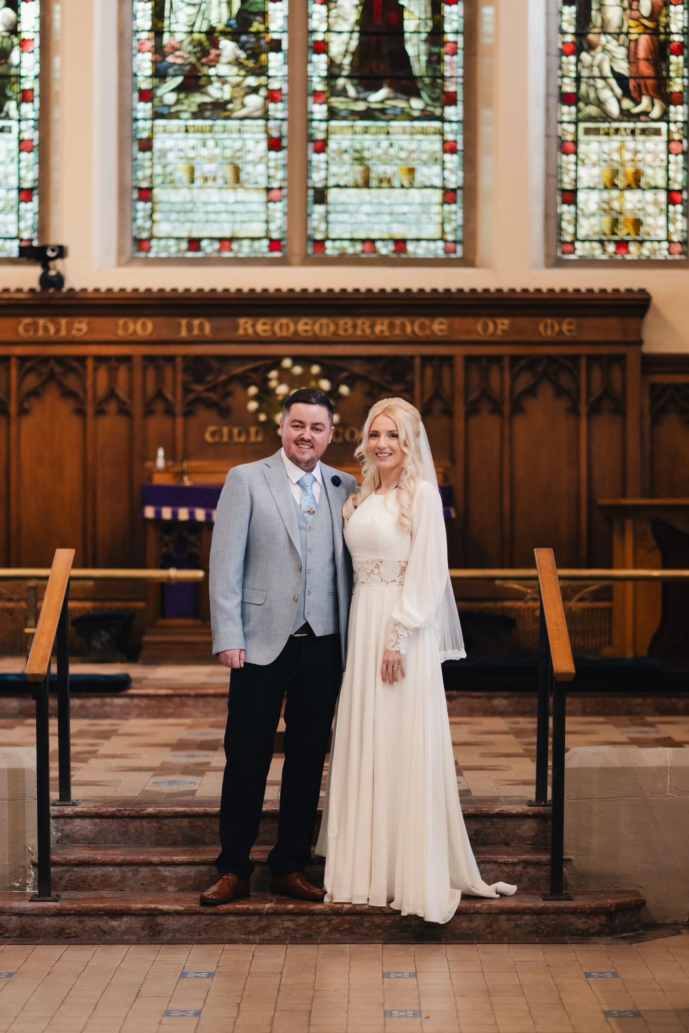 a bride and groom standing in front of a stained glass window