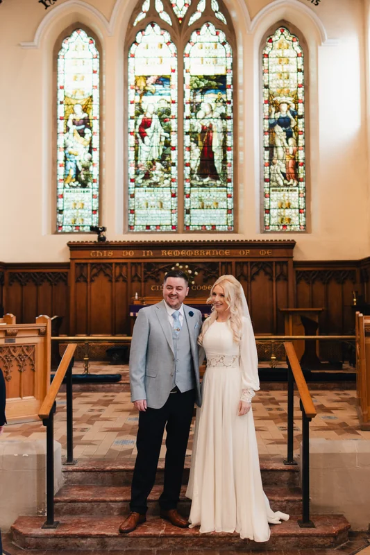 a bride and groom standing in front of a stained glass window