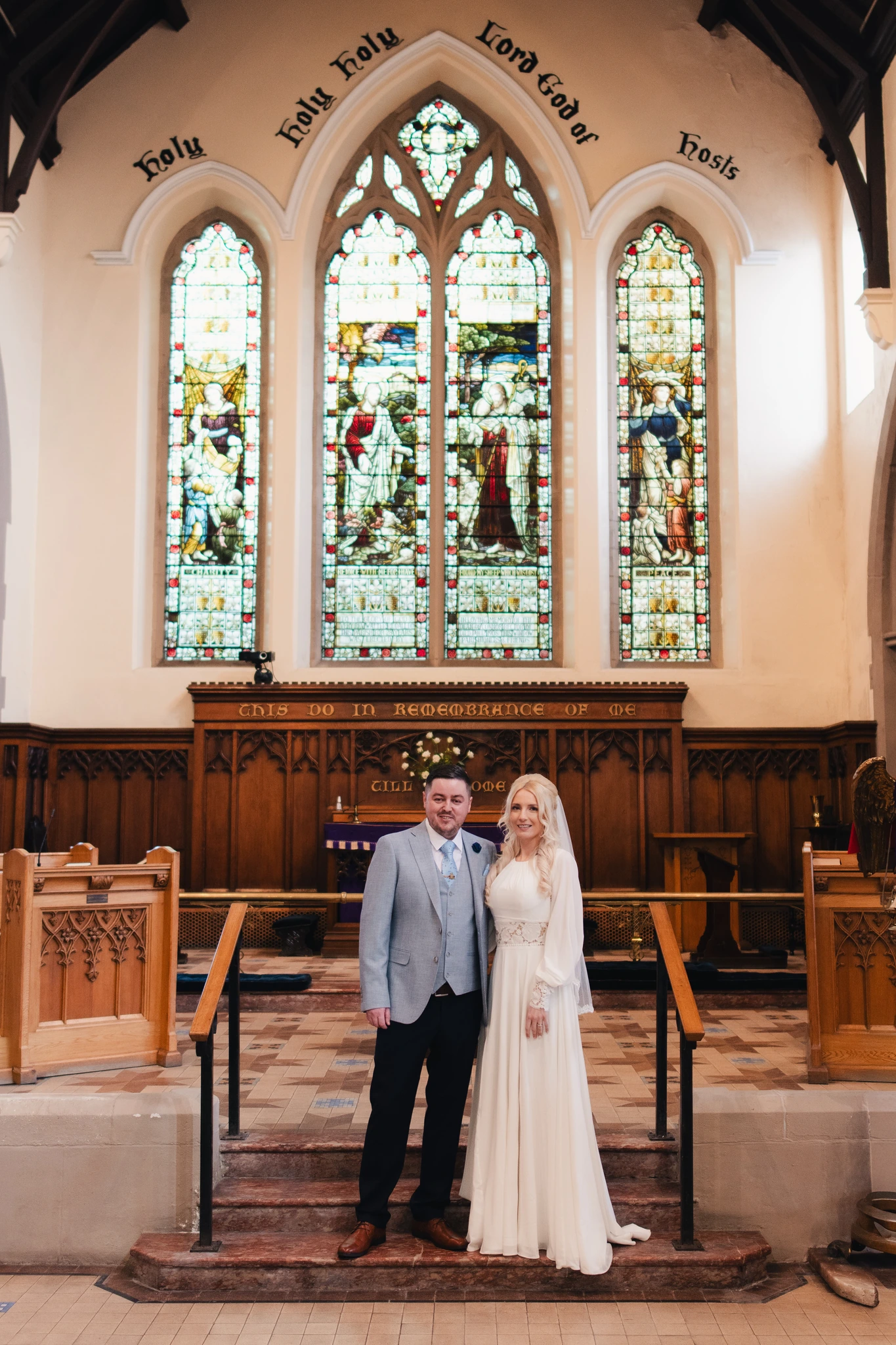 a bride and groom standing in front of a stained glass window in a church