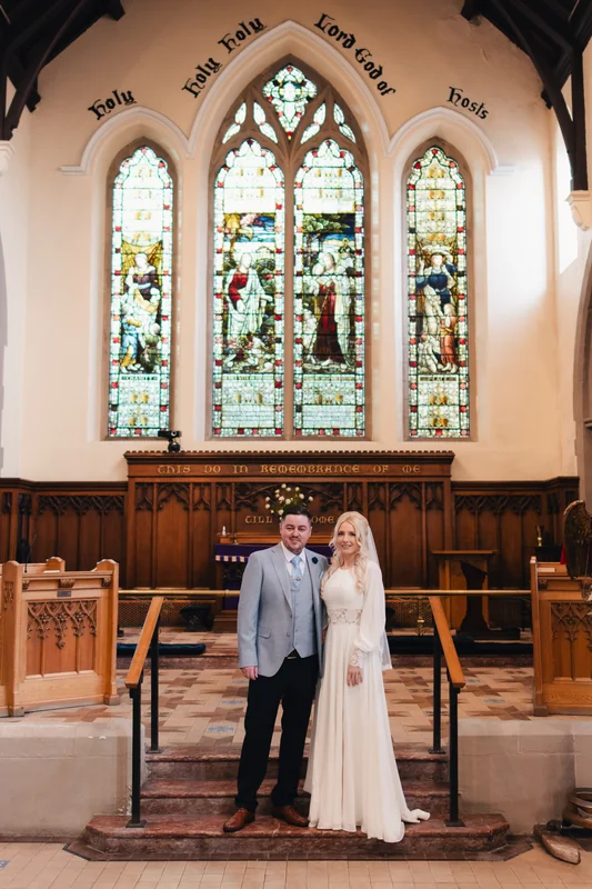 a bride and groom standing in front of a stained glass window in a church