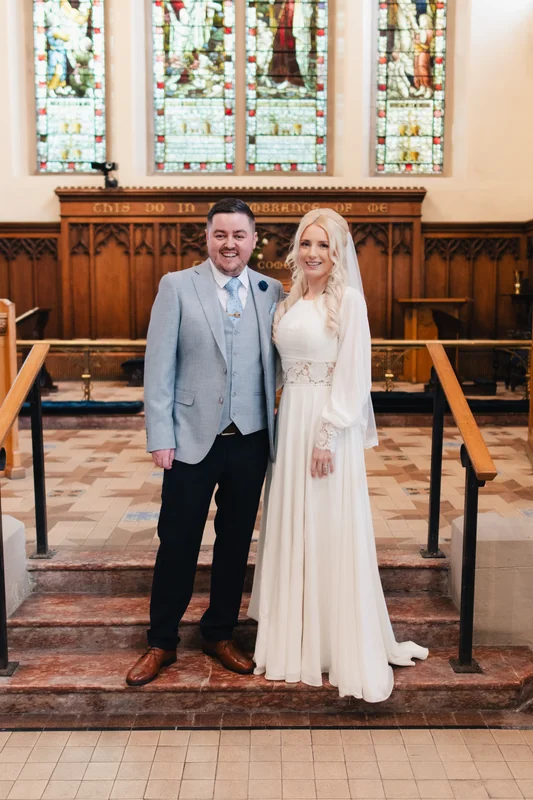 a bride and groom standing in front of a stained glass window