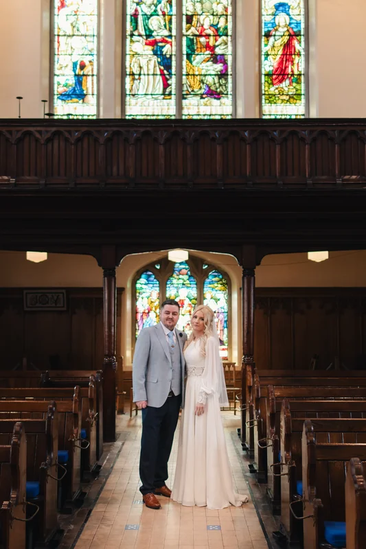 a bride and groom standing in front of a stained glass window