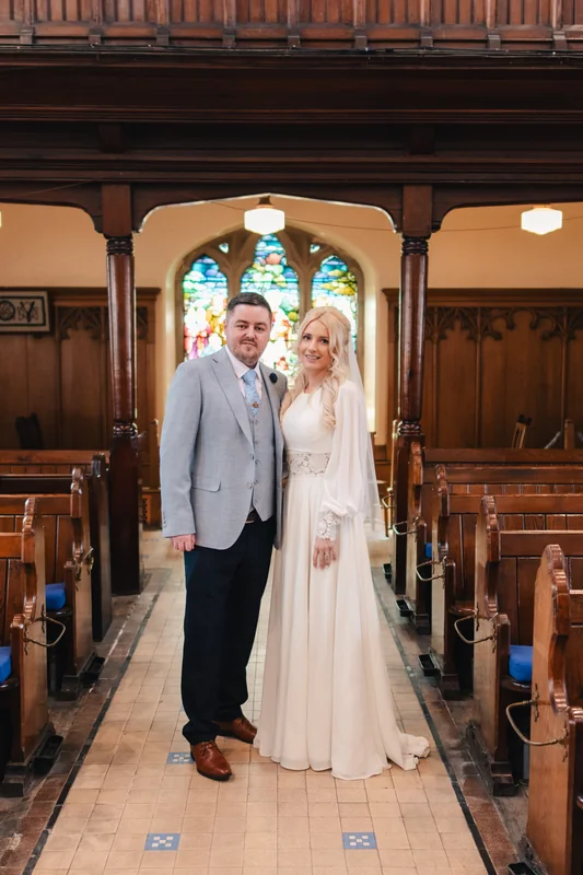 a bride and groom standing in front of a stained glass window in a church