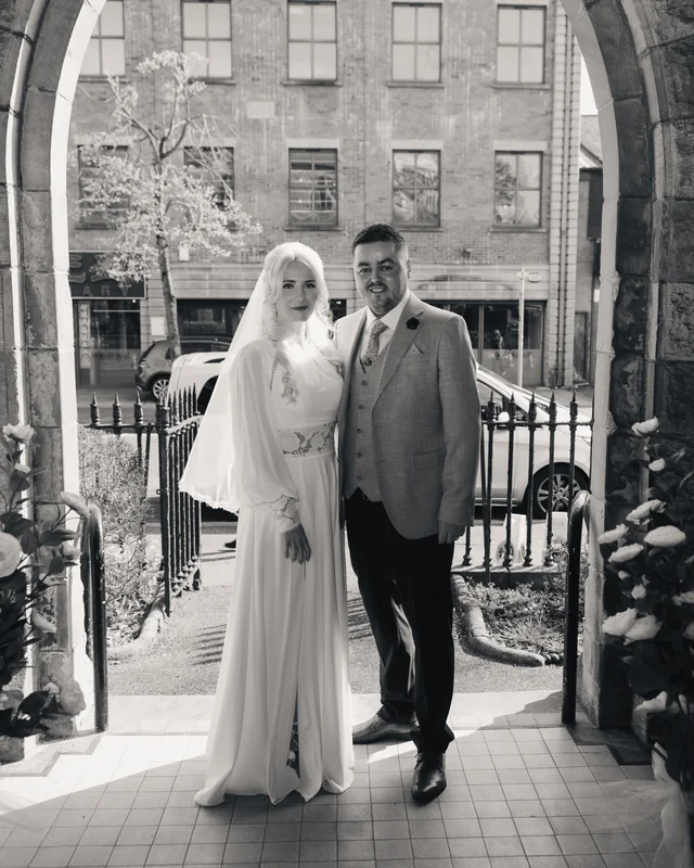 a bride and groom standing in front of an archway