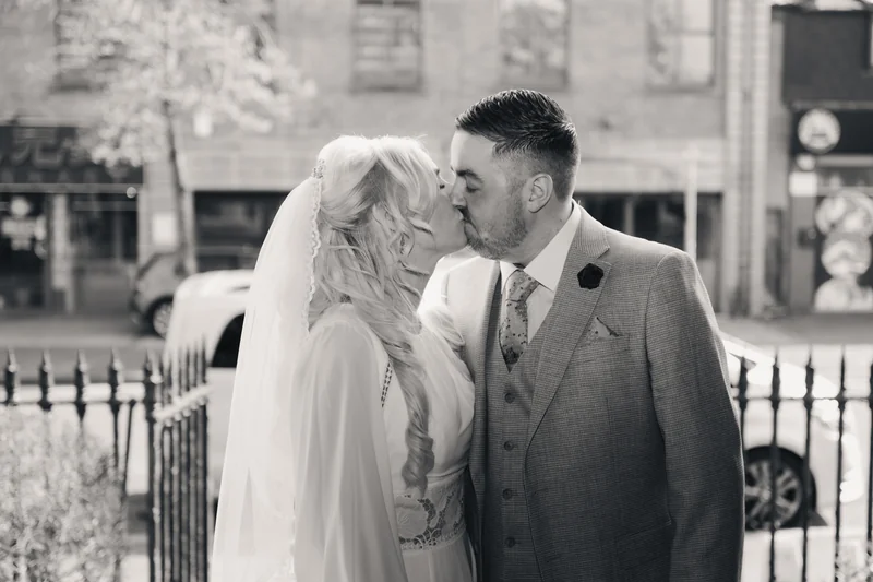 a bride and groom kiss in front of a black and white photograph