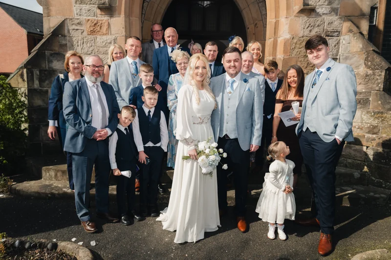 a bride and groom pose with their wedding party in front of a church