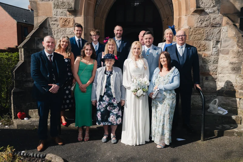 a bride and groom pose with their wedding party in front of a church