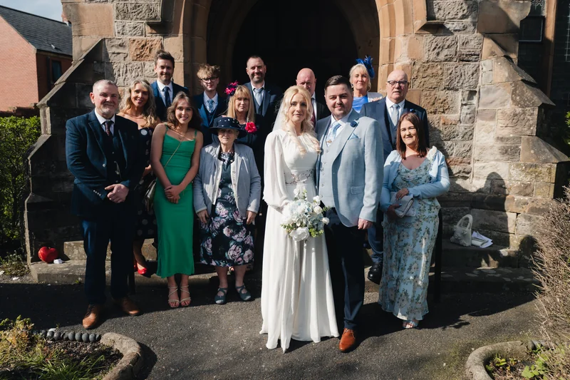 a bride and groom pose with their wedding party in front of a church