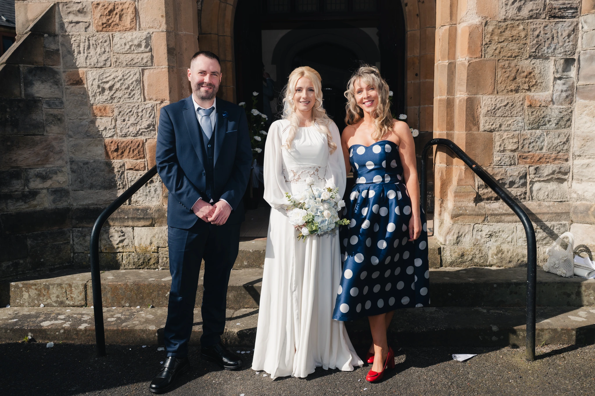 a bride and groom pose for a photograph in front of a church