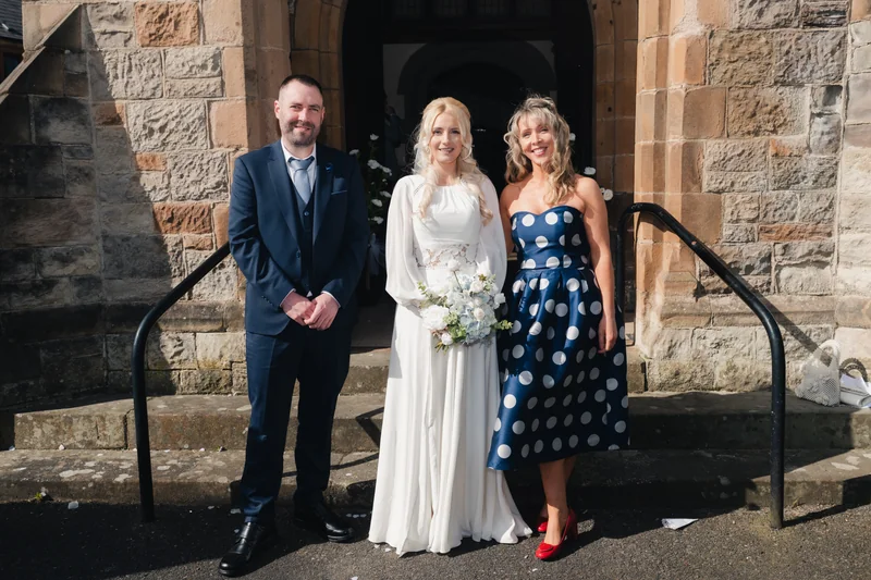 a bride and groom pose for a photograph in front of a church