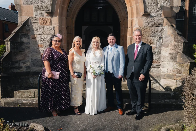 a bride and groom pose with their wedding party in front of a church