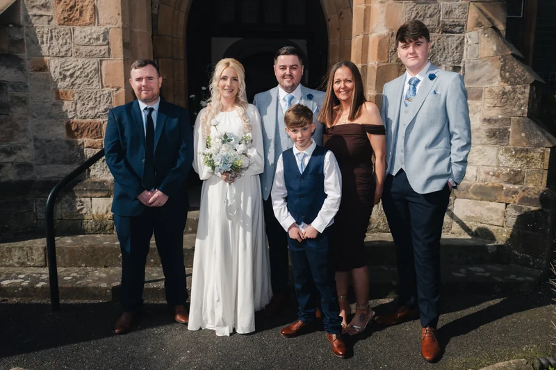 a bride and groom pose with their wedding party in front of a church