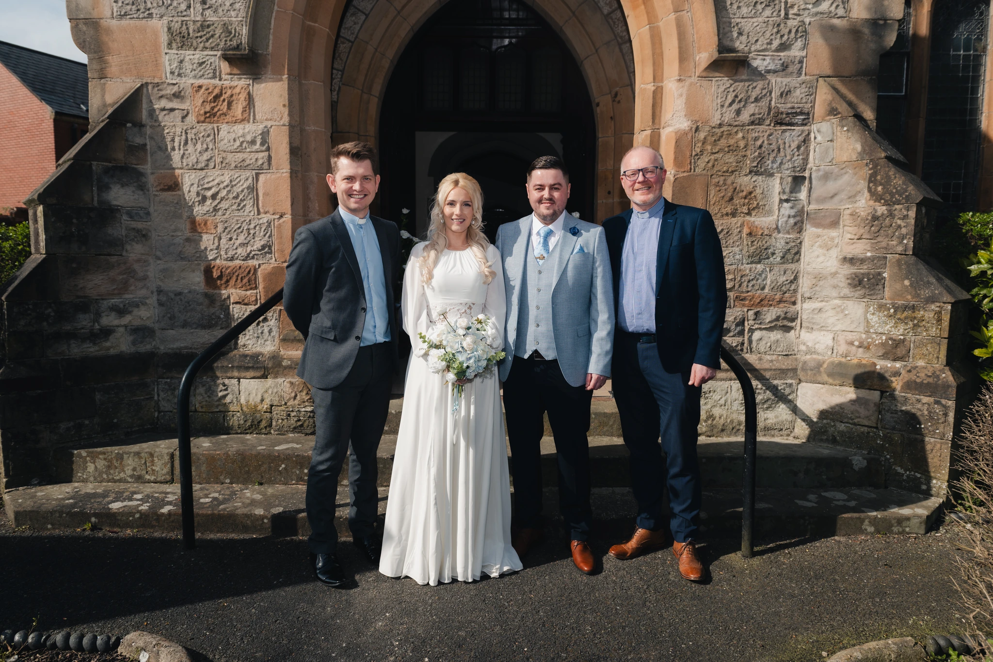 a bride and groom pose with their wedding party in front of a church