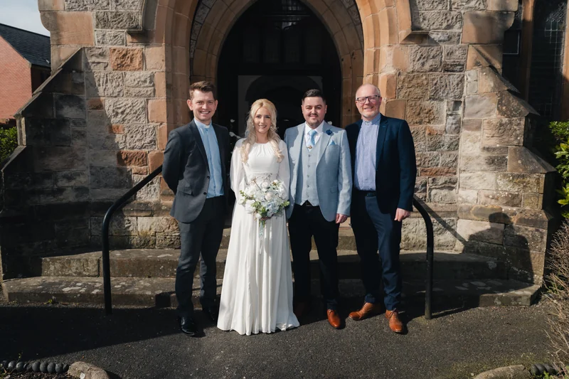 a bride and groom pose with their wedding party in front of a church