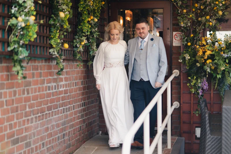 a bride and groom walk down the stairs of their wedding venue