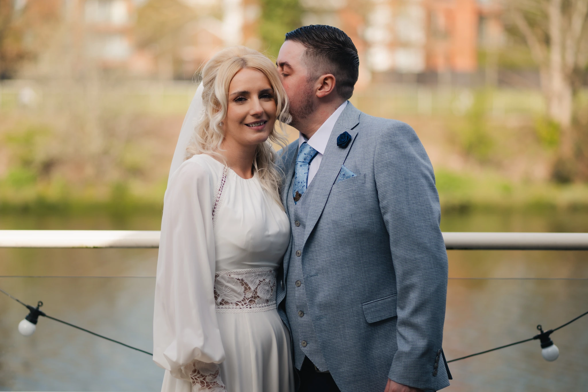 a bride and groom kiss on a balcony overlooking a river