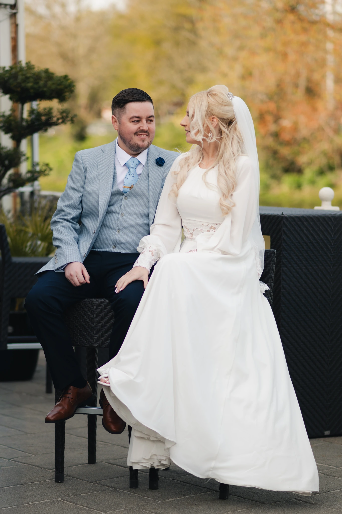 a bride and groom sitting on a wooden bench in a garden