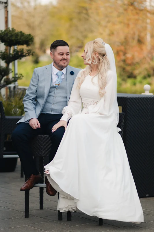 a bride and groom sitting on a wooden bench in a garden