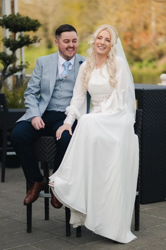 a bride and groom sitting on a wooden bench in a garden