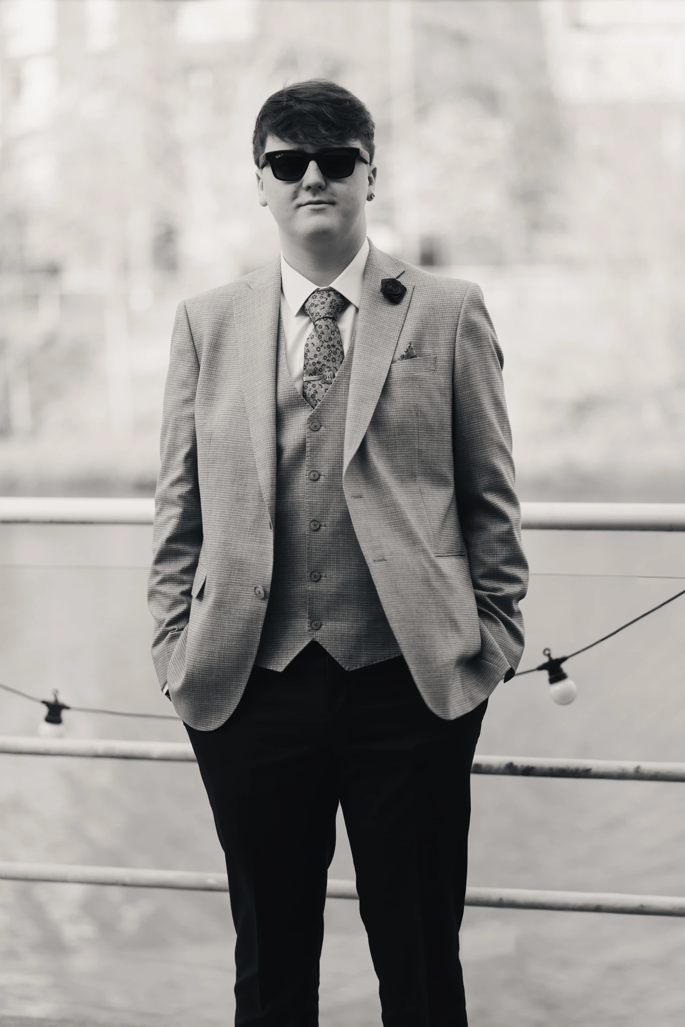a man in a suit and tie standing on a railing by a river