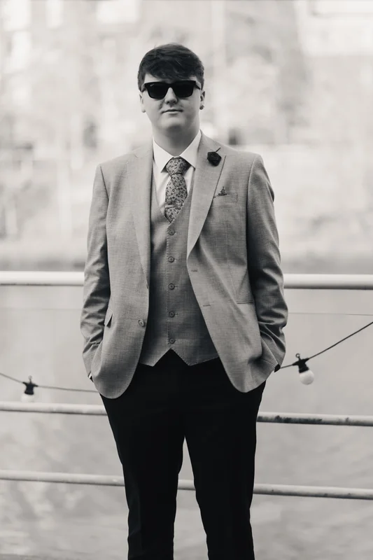 a man in a suit and tie standing on a railing by a river