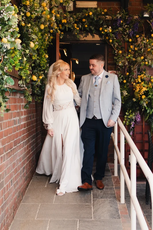 a bride and groom walk down the stairs of their wedding venue